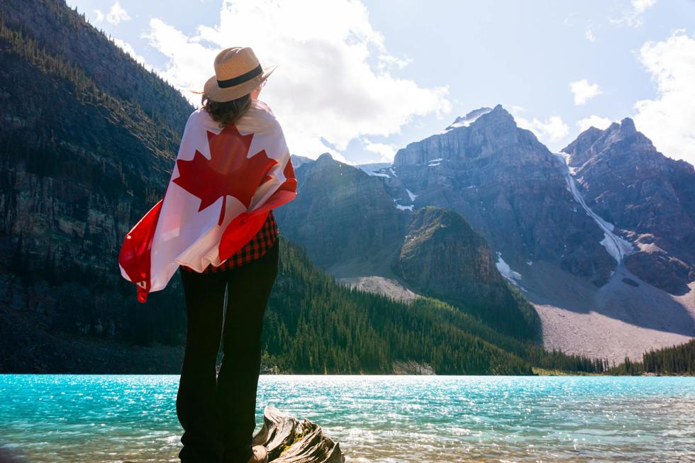Woman standing by Banff lake, wrapped in Canadian flag